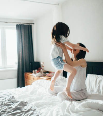 woman lifts her child up in joy while on her bed after a good nights rest